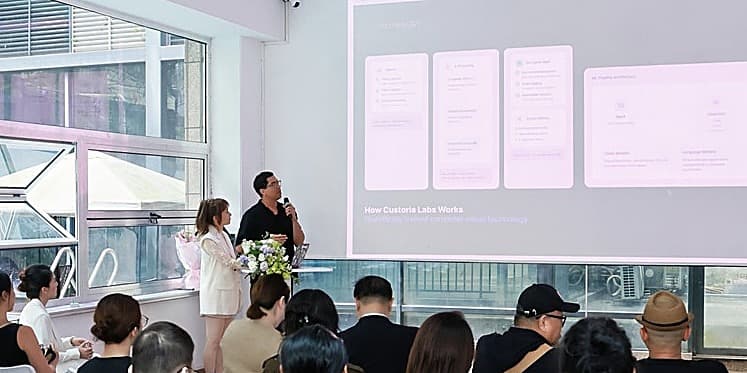 Anton Castro presenting 'How Custoria Labs Works' at a demo day, with co-founder Yiyi Qin beside him and a seated audience